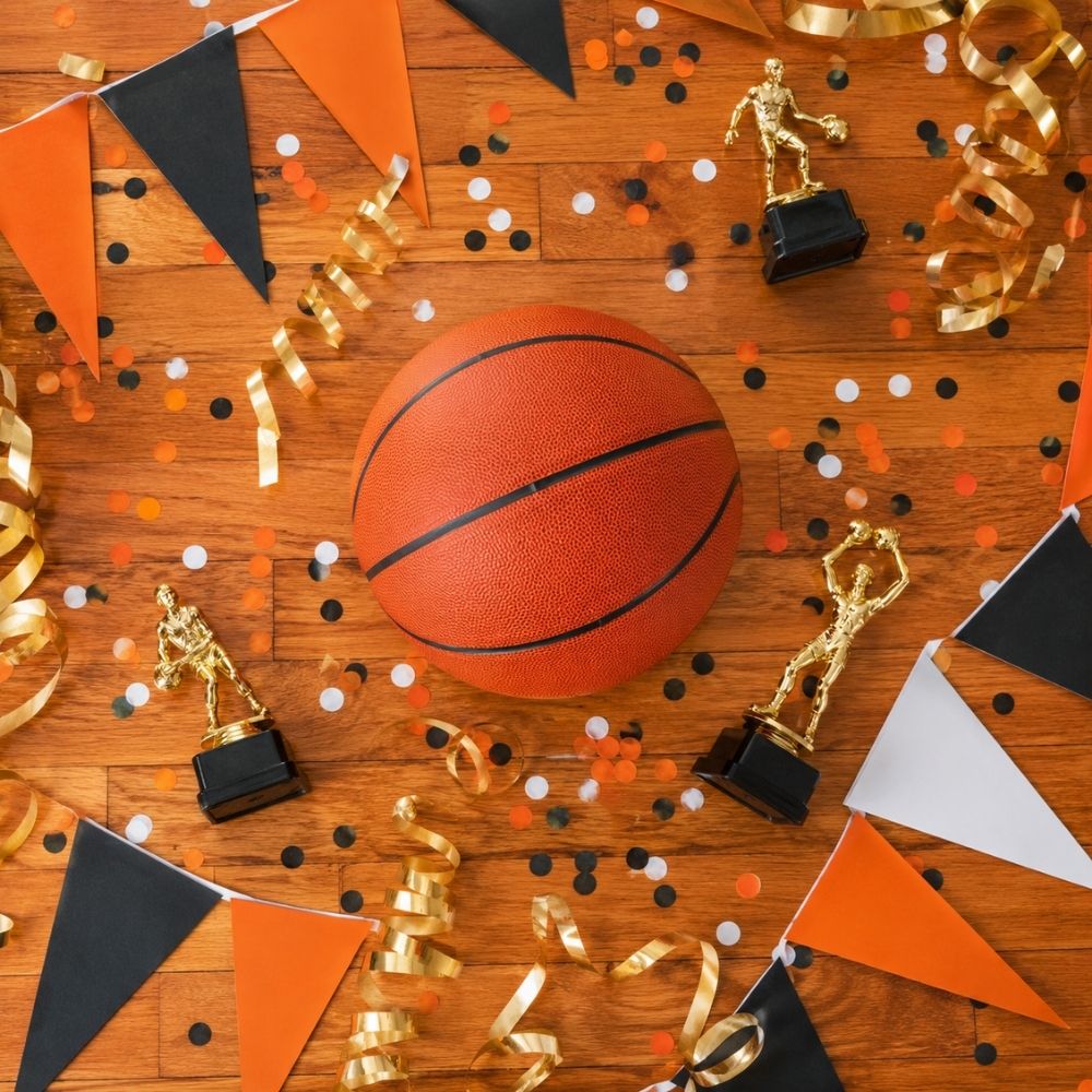 Overhead-Flatlay mit orangefarbenem Basketball, Konfetti und Pokalen auf glänzendem Parkettboden