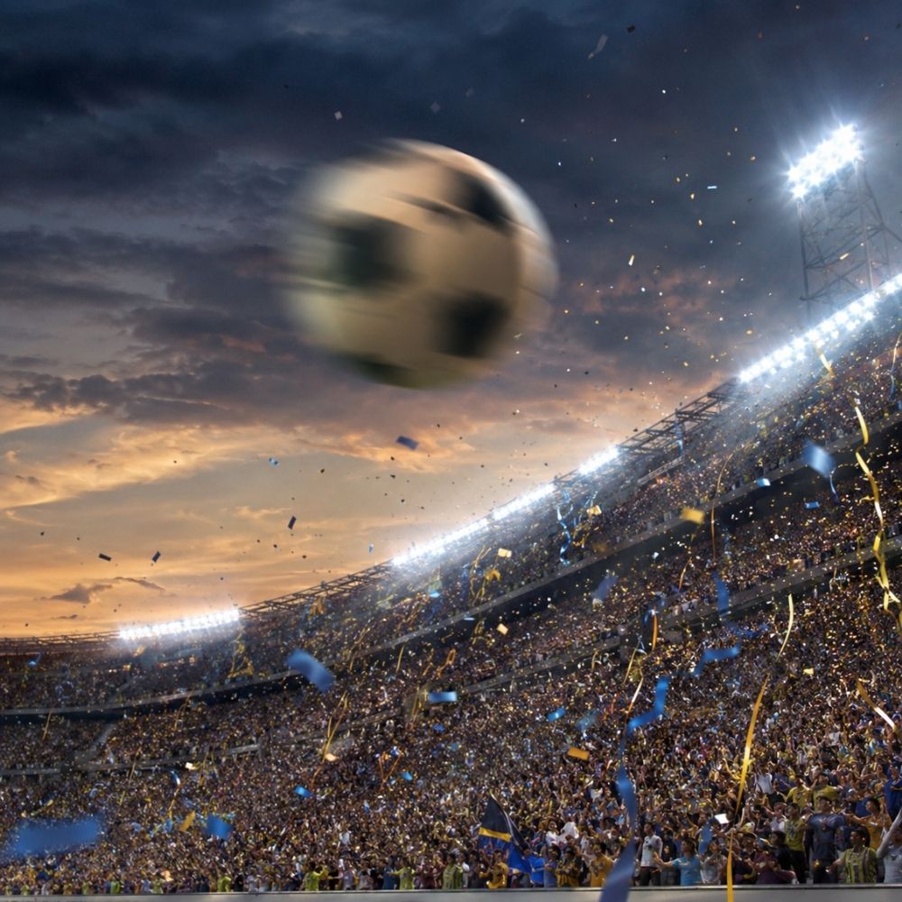 Dramatische Actionaufnahme eines fliegenden Fußballs über vollem Stadion mit Konfettiregen